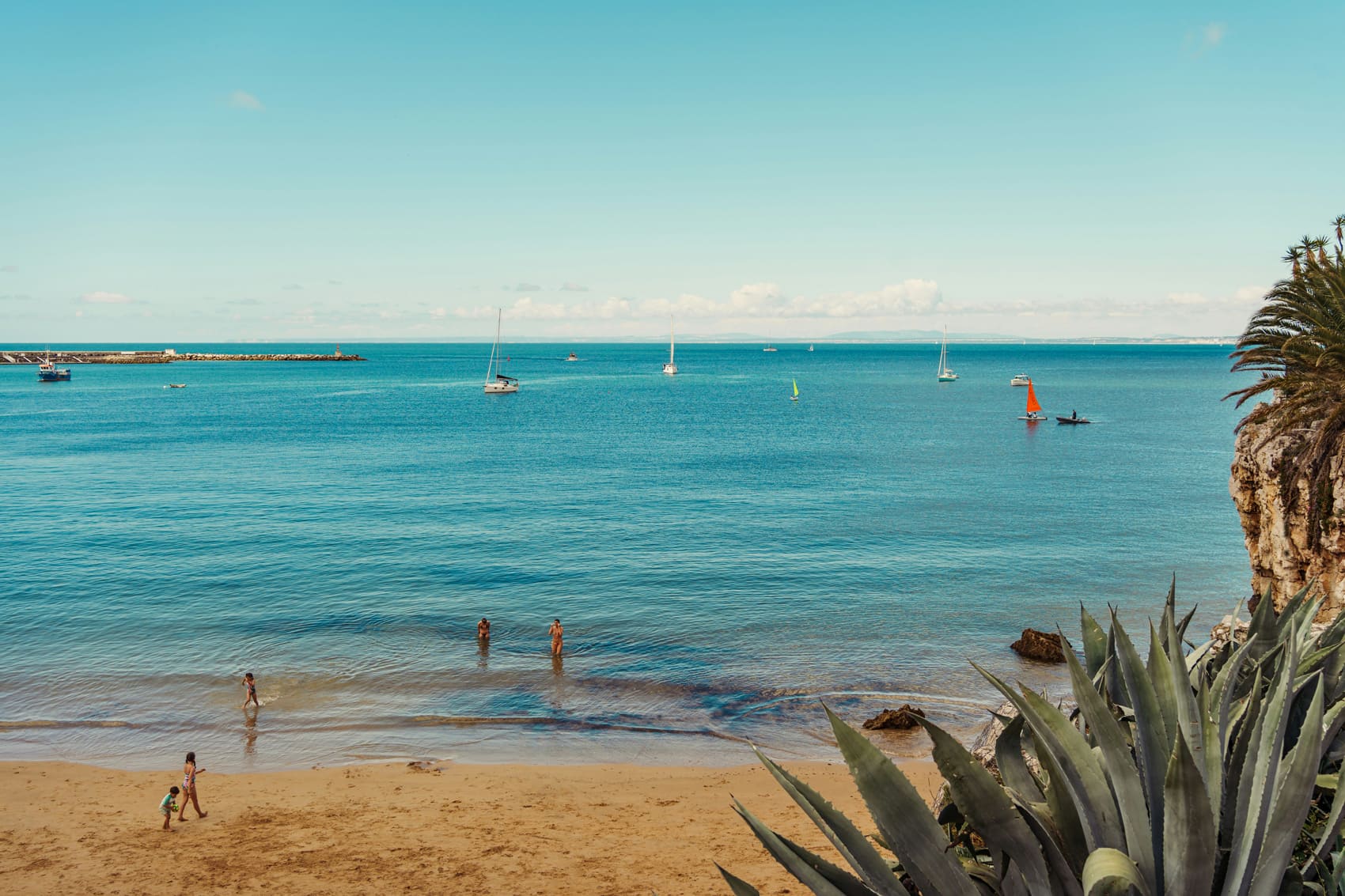 Plage et côte du Portugal avec mer turquoise, voiliers et falaises, illustration du cadre de vie des résidents fiscaux français au Portugal